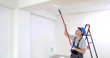 Tecrübeli ve yetenekli bir ressam yeni yenilenmiş bir odanın tavanını boyamak için ustalıkla bir silindir kullanıyor.