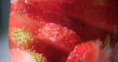 Çilek parçaları temiz suyla dolu şeffaf bardakta yüzer. Ev yapımı smoothie için malzemeler. İnce çilek dilimleriyle dolu bir kap.