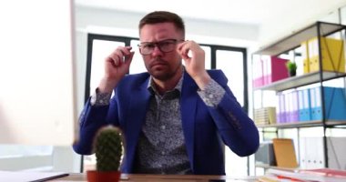 Mavi takım elbise giymiş odaklanmış bir adam modern çalışma ortamında gözlüklerini dikkatlice ayarlar.