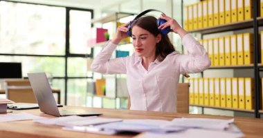 Işıl ışıl bir ofis ortamında oturan genç bir kadın, kulaklık takarken işiyle mücadele ediyor.