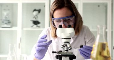 Kendini işine adamış bir kadın bilim adamı mikroskopla detaylı analiz için kuyuda örnekler inceliyor.