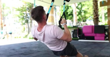 Açık hava spor salonunda bir adam TRX gösterileri yapıyor. Gücünü ve kondisyonunu gösteriyor.
