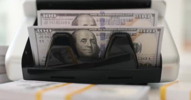 Para sayma makinesi masasında 100 dolarlık banknotlarla çalışıyor. Bankacılık ekipmanları, ofisteki para transferlerinin hassasiyetini sağlıyor