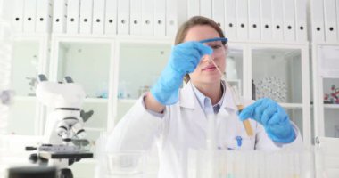 Cam çubuklu laboratuvar teknisyeni test tüpünde sıvı karıştırıyor. Gözlüklü kadın kimyager laboratuardaki tepkimeyi test etmek için renk sıvısını karıştırıyor.
