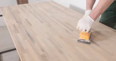 Eldivenli işçiler ahşap tahtayı el yapımı elektrikli zımpara makinesiyle cilalarlar. Tamirci, masa yüzeyini modern ahşap işçiliği aracıyla kapalı alanda işler.