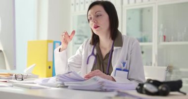 Kadın doktor, klinikteki evrak işlerinden bıktığını belirterek alnına dokunuyor. Doktor hasta geçmişleriyle uğraşmaktan yoruldu.