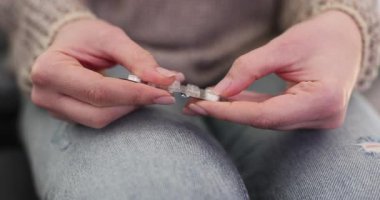 Kadın elleri koltukta oturan su toplayıcı paketten tablet çıkarır. Kot pantolonlu bir kadın evde hastalık belirtileriyle başa çıkmak için ilaç hazırlıyor.