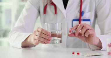 Kadın doktor masanın üzerinde bir bardak su ve ilaç kapsülü tutuyor. Doktor, hastanedeki hastalıkları tehdit etmek için reçeteli ilaç verilmesini öneriyor.