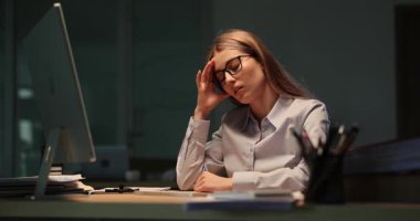 Yorgun kadın ofis çalışanı gece geç saatlere kadar masa başında oturur. Gözlüklü yorgun iş kadını yarı karanlıkta görevini tamamlamaya çalışıyor.