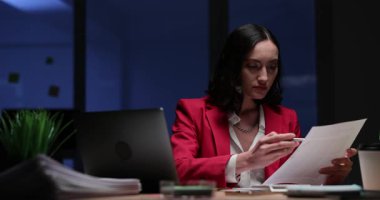 Odaklanmış kadın, gece geç saatlerde ofiste çalışırken yapılan hatalar için mali raporları kontrol ediyor. Bayan yönetici iş ortamında şirket belgelerini hazırlar.