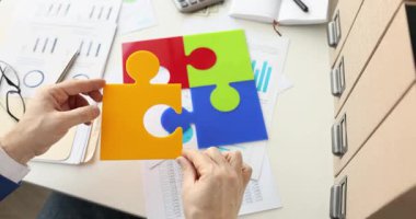 Ekip çalışanı büyük parlak yapbozun son parçasını ağır çekimde masaya yerleştiriyor. Resmi takım elbiseli bir profesyonel ofis odasında şirket görevini tamamlıyor.