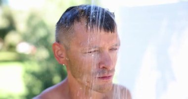 Üç günlük ahırı olan adam kır evinde duş alıp saçlarını yıkıyor. Rahatlamış erkek yaz günü plaj aktivitelerinden sonra suyla serinliyor.