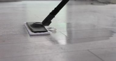 Ev hanımı buharlı paspas ve döşemeleri temizliyor. Temizlikçi yağ lekelerini temizlemek için buharlı süpürgeyi ileri geri hareket ettiriyor. Yavaş çekim