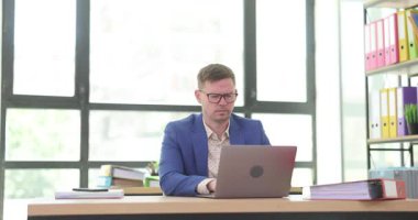 Gözlüklü, konsantre bir ofis çalışanı ofiste dizüstü bilgisayarla çalışıyor. Kadın sekreter bilgisayardan bilgi almaya çalışıyor.