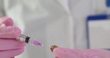 Eldivenli doktor şırıngayı küçük altın cam şişenin yanında tutuyor. Laboratuvarda maddenin enjekte edilmesini içeren tıbbi bilimsel prosedür