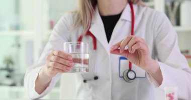 Paltolu kadın doktor elinde hap ve bir bardak su tutuyor. İlaç yönetimi, hastanede sağlık ve hasta bakımını ima ediyor
