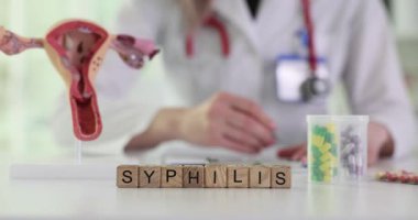 Doktor frengi kelimesinin yanındaki kağıtlara tahta bloklara ve masadaki haplarla dolu rahim modeline yazı yazıyor. Tıbbi bağlamda tedavi