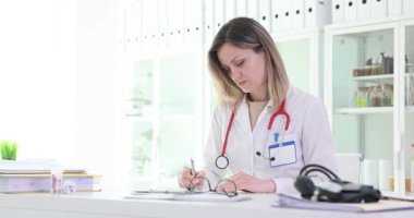 Kadın doktor masasına parlak steteskop yerleştirip masadan kalkar. Yorgun kadın, modern hastanedeki zor vardiyanın sonunu simgeliyor.