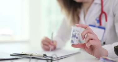 Bayan doktor panoya yazı yazarken elinde küçük bir ilaç şişesi tutuyor. Sağlık hizmetleri ortamında tıbbi danışmanlık reçetesi ve belgeler