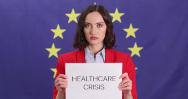 Genç kadın, Avrupa Birliği bayrağına karşı Sağlık Krizi tabiriyle bir kağıt tutuyor. İşaretteki mesaj, sağlık hizmetlerinin durumu hakkında ciddi endişelere işaret ediyor