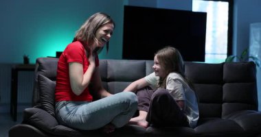 Anne ve kızı, karanlık odada şakalarını paylaşırken kahkahalara boğuldular. Kadınlar aptalca şakalara kontrolsüzce gülerek kanepeye yaslanırlar. Yavaş çekim