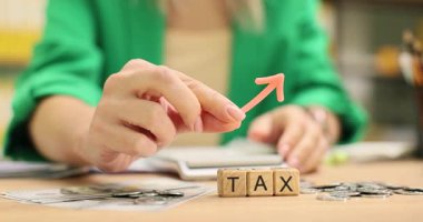 Ceketli bir kadın, tahta blokların tepesine kelime vergisiyle küçük bir ok yerleştiriyor. Ofiste etrafa saçılmış madeni paralar maddi meseleleri işaret ediyor