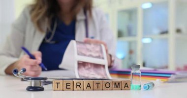 Masasında Teratoma yazan tahta bloklar ve ultrason görüntülerini tutan palto ve steteskoplu bir kadın. Patolojiyle ilgili tıbbi içerik