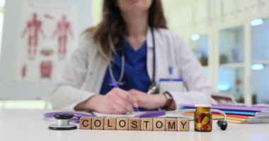 Palto ve steteskop giymiş genç bir kadın masadaki kağıtlara kolostomi ile ilgili bilgiler yazıyor. Sindirim sağlığıyla ilgili tıbbi içerik