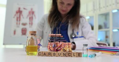 Kadın doktor masadaki belgelere tıbbi malzemelerle birlikte Carbuncle 'ı gösteren bloklar da yazıyor. Cilt enfeksiyonu hakkında bilgi araştırması