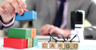 Adam, masanın üzerinde kelime kargosunun yanına minyatür konteynır piramidi inşa ediyor. İş adamı uluslararası nakliye konseptini sundu