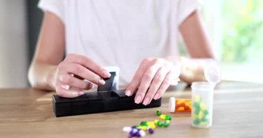 Kadın ilaç organizatörünü ahşap masada oturan renkli kapsüllerle dolduruyor. Bayan evde plastik konteynırda günlük dozda ilaç hazırladı.