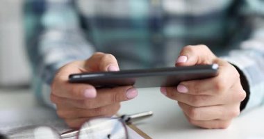 Kadın ofis sandalyesinde oturuyor ve telefonda mobil oyun oynuyor. Kareli tişörtlü kadın çalışan öğle arasında rahatlamak için oyuna odaklanıyor. Yavaş çekim