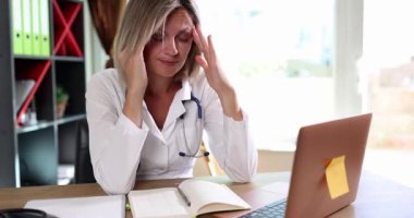 Kadın doktor baş ağrısından kurtulmak için şakaklarına masaj yapıyor. Yorgun suratlı bir doktor yorgunluktan kaynaklanan acıyı azaltmaya çalışır. Yavaş çekim