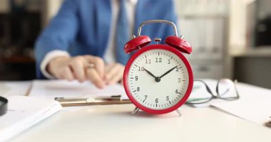 İş adamına karşı çalar saat ofis masasındaki belgeleri kontrol ediyor. Şirket yöneticisi sözleşmeyi okumak için acele ediyor ve son teslim tarihinden önce hataları düzeltiyor