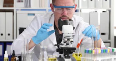 Ciddi adam kimya laboratuvarında mikroskopla test tüpünde sıvı numunesi üzerinde çalışıyor. Bilim adamı modern ekipmanları kullanarak renk çözümleri üzerinde çalışıyor