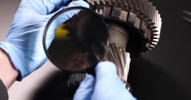 Büyüteçli tamirci dükkandaki tezgahta araba şanzıman şaftını kontrol ediyor. Teknisyen, araba istasyonundaki metal otomobil detaylarında hasar izleri istiyor.