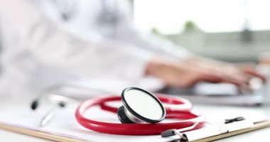 Konsantre doktor masada oturur ve dizüstü bilgisayarına tıbbi notlar yazar. Stetoskop ve tıbbi evraklar düzgünce masaya yerleştirilmiş. Yavaş çekim