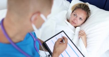 Doktor koğuşta elinde tablet olan hasta kadının endişelerini dinliyor. Erkek doktor semptomlar hakkında not alır ve uygun tavsiyelerde bulunur.