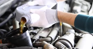 Eldivenli tamirci motor yağını açık araba kaputunun altında değiştiriyor. İşçi, ağır çekimde otomobil deposuna sıvı kehribar yağı döküyor.