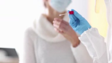 Doktor steril pamuk çubuğu tutuyor ve hasta bayanın burun deliğine sokuyor. Koruyucu eldivenli doktor daha fazla analiz için burun örneği topluyor.