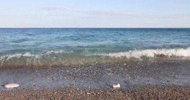 Çalkantılı gök mavisi deniz ve ıssız bir yerde kumlu sahil. Turkuaz dalgalar ufukta görünen dağ zirvelerine karşı kıyıya vuruyor.