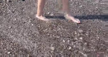 Çakıl taşlı sahilde çıplak ayakla yürüyen kadın bacakları küçük dalgalarla yıkandı. Bayan tatil boyunca sahilde deniz esintisi ve ılık suyu sever.