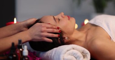 Masaj terapisti, kadının alnını saçının yanında nazikçe okşar. Müşteri rahat bir salonda mumlarla profesyonel masaj sırasında dinlenir ve dinlenir.