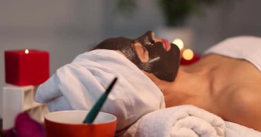 Kadın kaplıca salonunda yüzü kilden maskeyle yatıyor. Keyifli tedaviler sırasında mumlarla dinlenmek rahat ve rahat bir ortam yaratır.