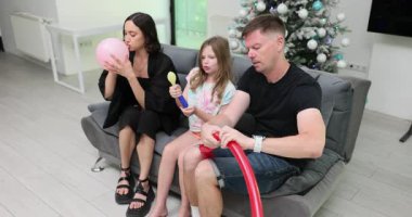 Anne ve baba çocuğuyla kanepede oturur. Annem derin bir nefes alıyor ve pembe balonu şişirmeye başlıyor. Kız sarı balonu şişirmek için pompa kullanıyor