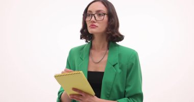 Gözlüklü kadın beyaz arka planda hoparlör dinliyor. Kadın dersten önemli noktalar yazıyor. Yavaş çekim