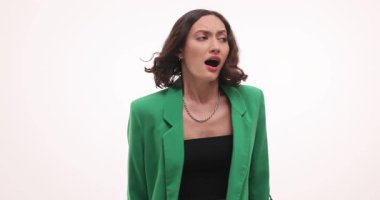 Çığlık atan kadın elleriyle başını tutuyor ve panikle beyaz arka plana bakıyor. Kadın uzayı geniş gözlerle tarar. Yavaş çekim