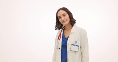 Palto giyen kadın doktor avuçlarını açıp teçhizat verirken nazikçe gülümser. Hastanedeki beyaz duvarın yanında bir kadın var.