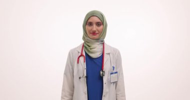Tesettürlü ve ceketli kadın doktor elinde bir kutu hap ve boş reçete defteri tutuyor. Müslüman kadın ışık odasında gülümsüyor