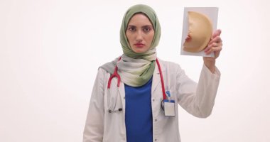 Tesettürlü kadın pembe kurdele ve göğüslerinin anatomik modelini elinde tutuyor. Ciddi ifadeye sahip Müslüman doktor kanser önleme çabalarını destekliyor